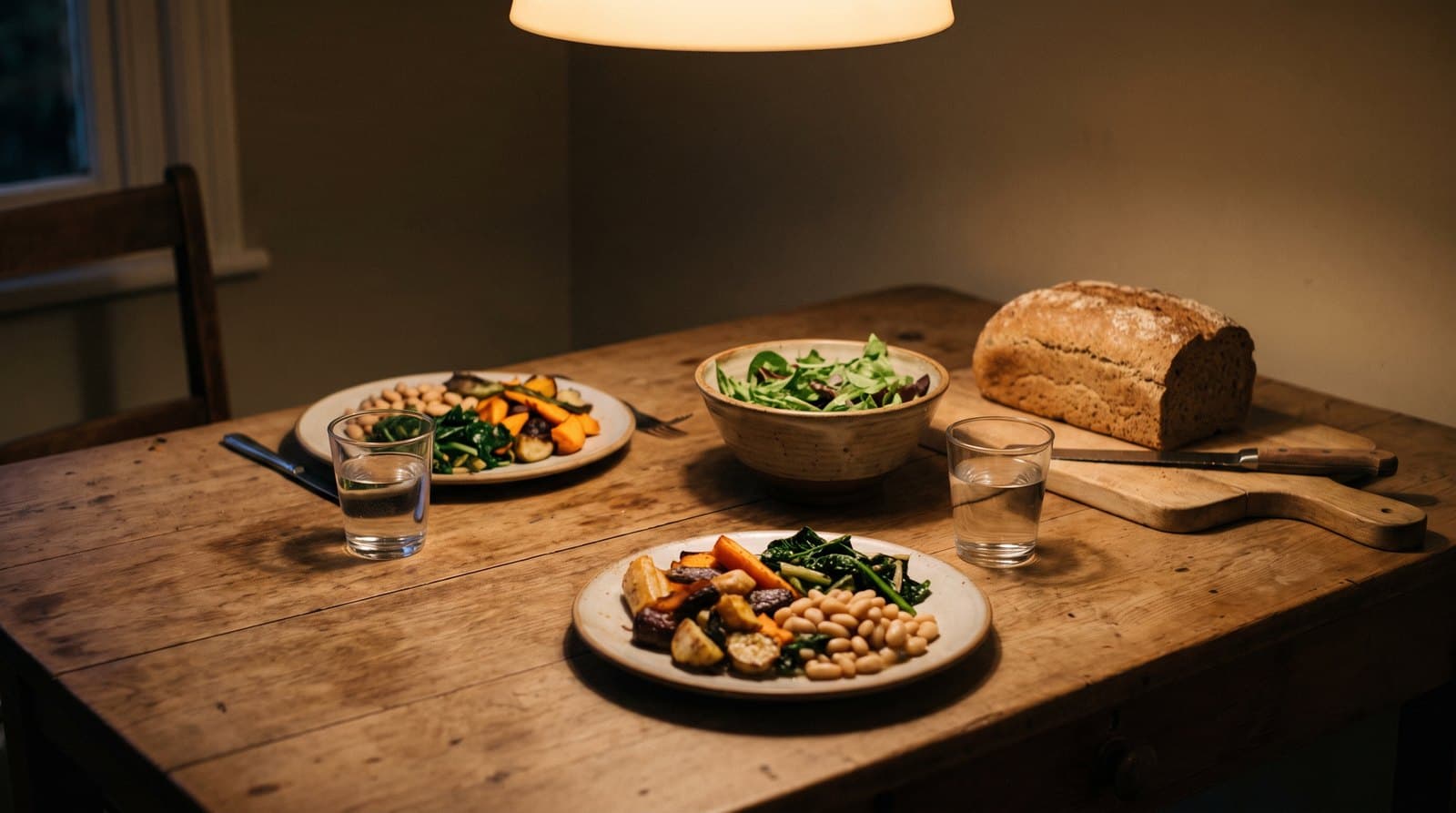 Dîner simple pour deux sur une table en bois : légumes rôtis, haricots blancs, salade verte, pain complet et verres d'eau
